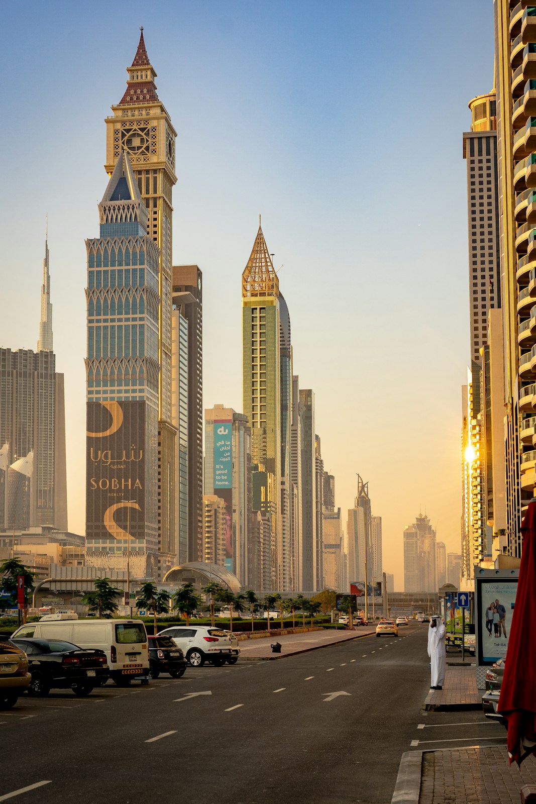 A person in a white thobe standing on a street in Dubai at golden hour
