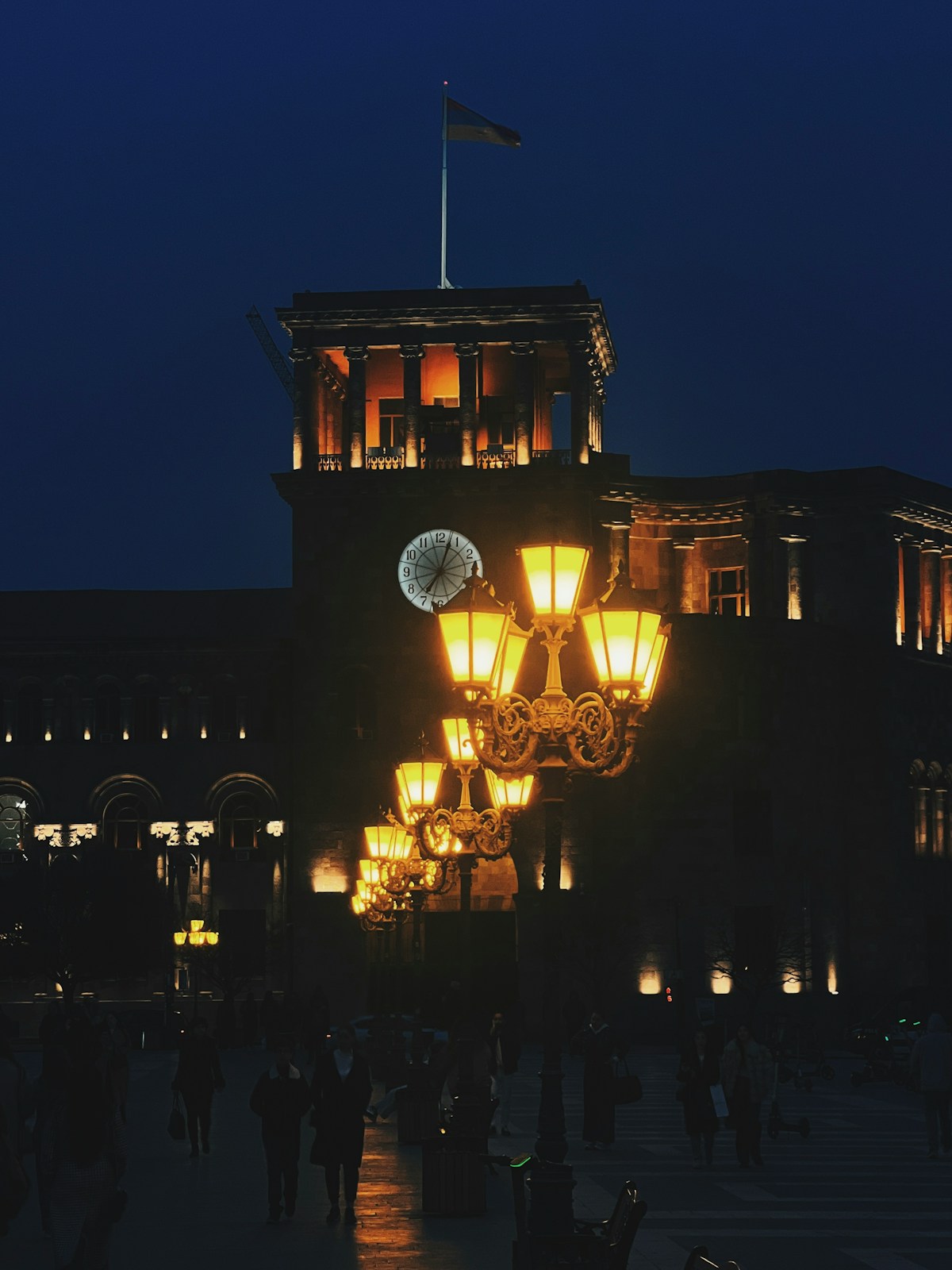 Ornate street lamps glowing in a square before a clock tower at night