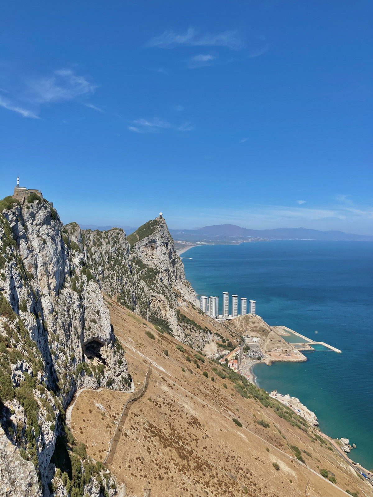 Rocky cliff overlooking the sea with buildings and distant mountains