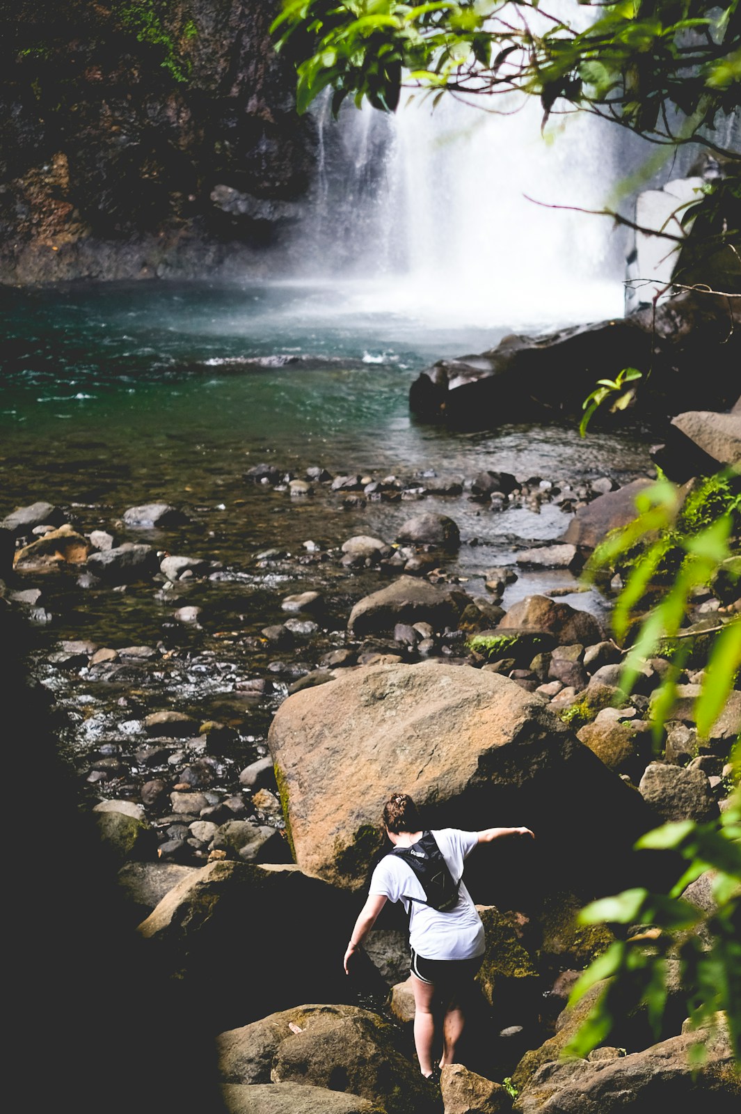 person walking on rocks near waterfall