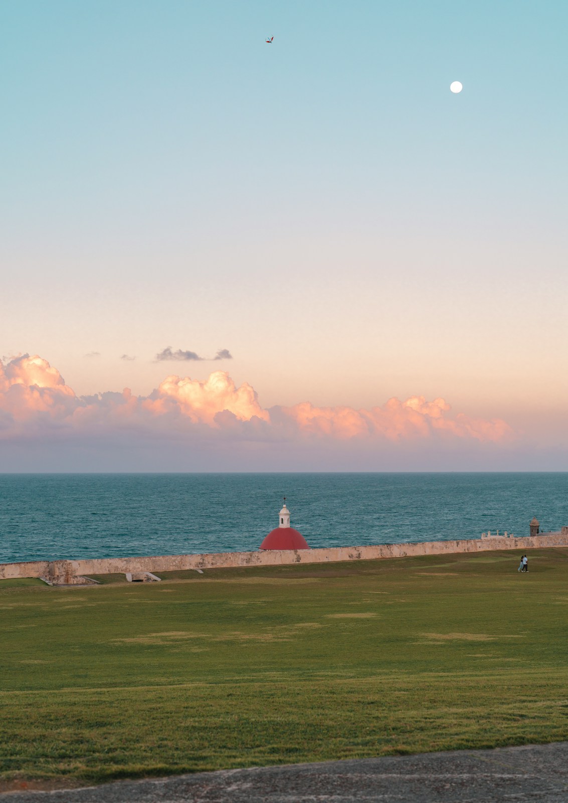 Pastel sunset over ocean, green field, and historic red dome
