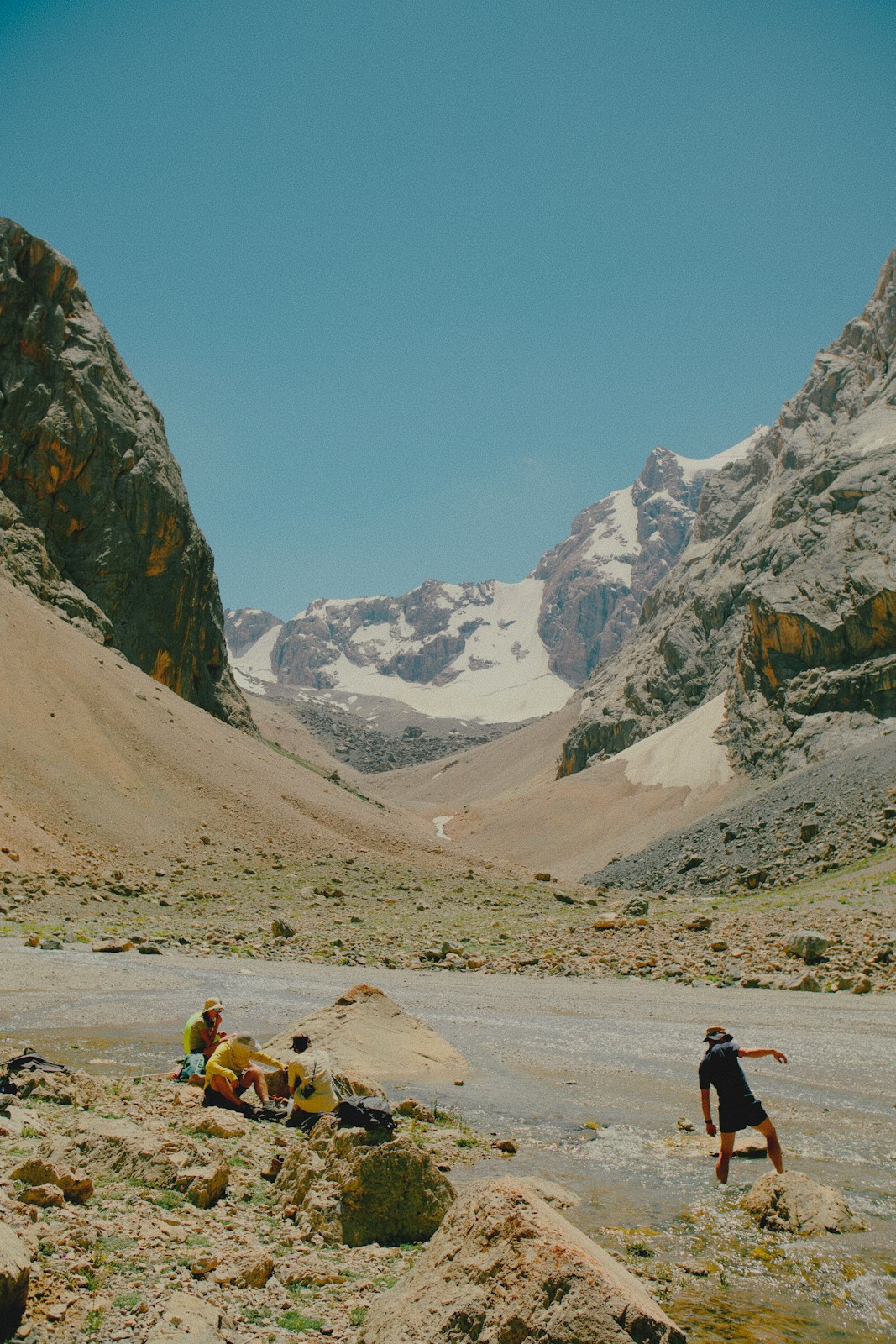 A group of people resting on rocks near a stream in a mountain valley