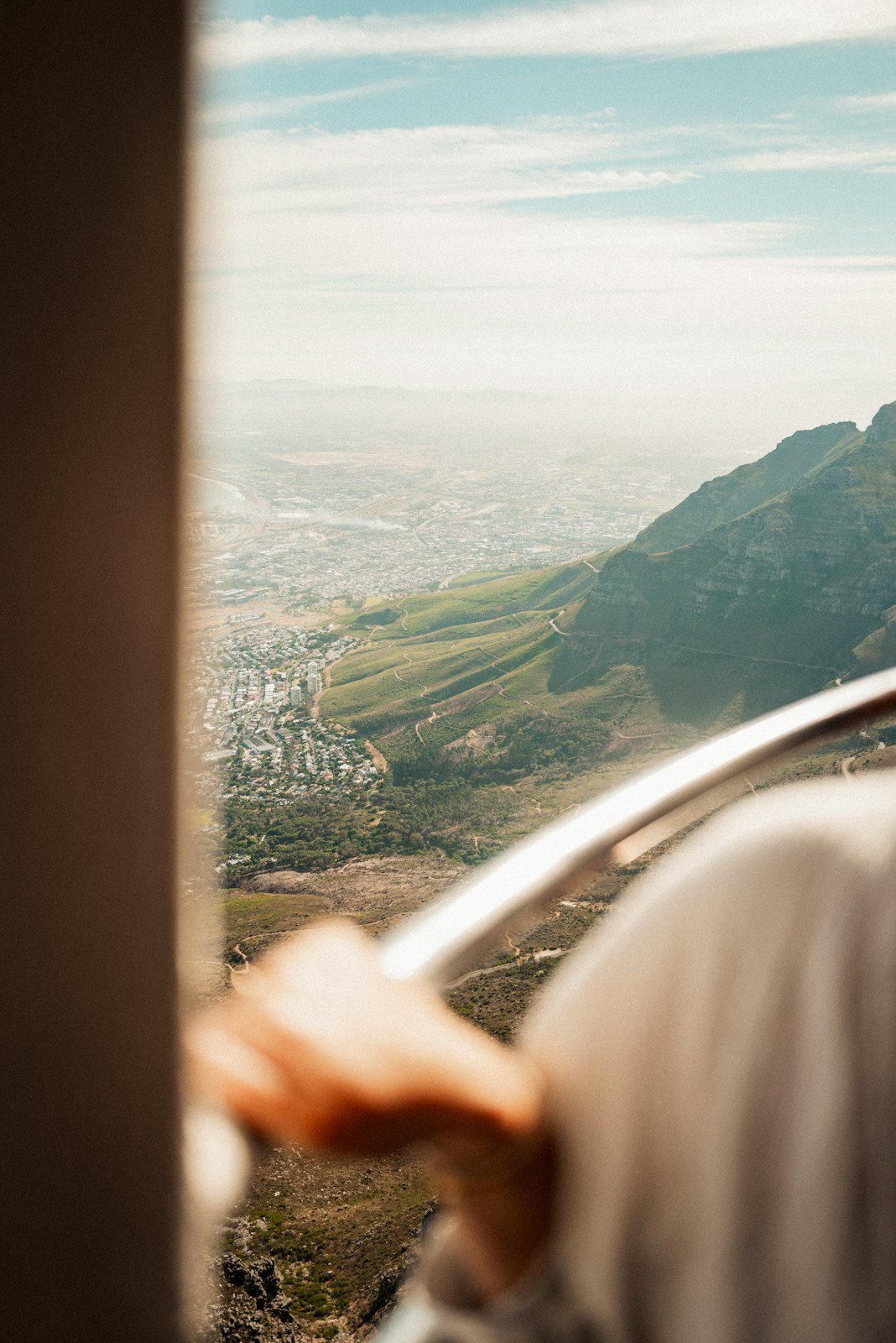 View of city from mountain with person's hand